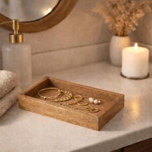 Wooden vanity tray holding gold jewelry on bathroom counter