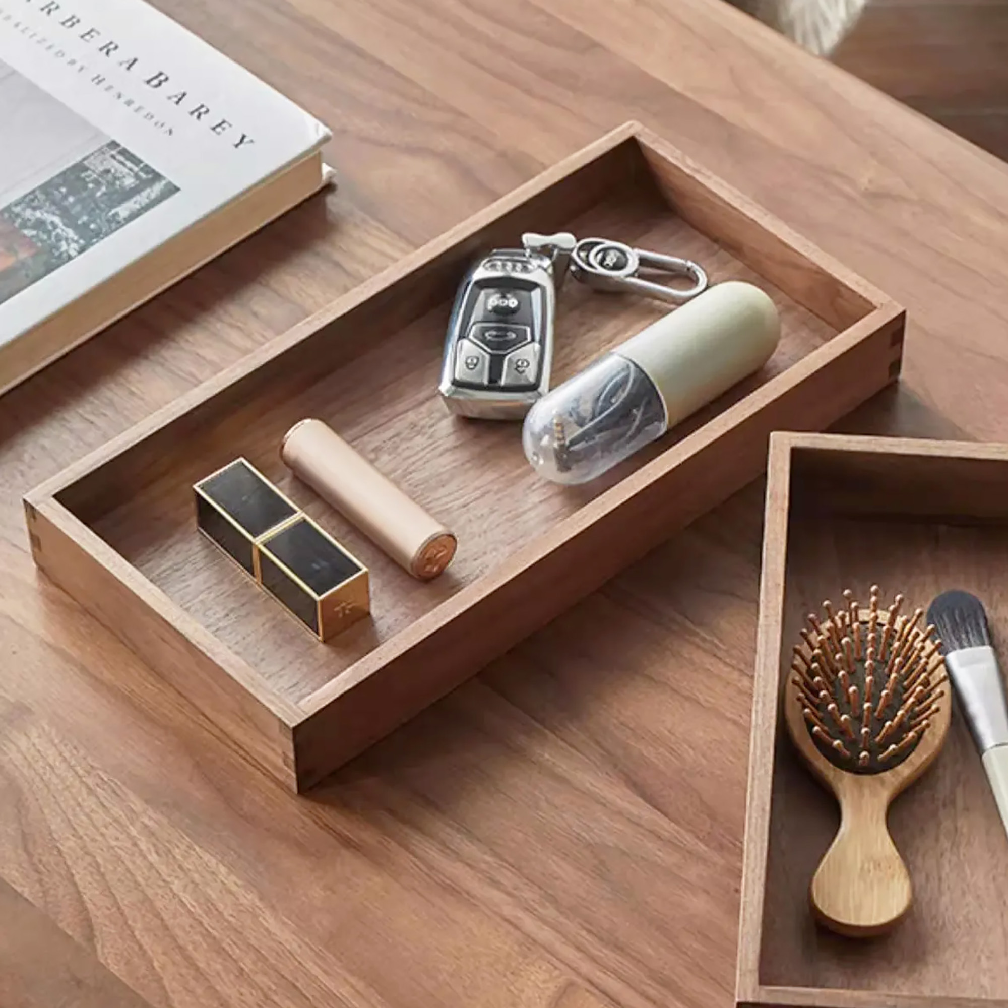 A wooden tray holding keys, lipstick, and accessories on a wooden surface.