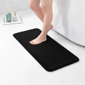 Barefoot stepping on a long black runner mat with pebble texture placed on a bathroom tile floor next to a tub