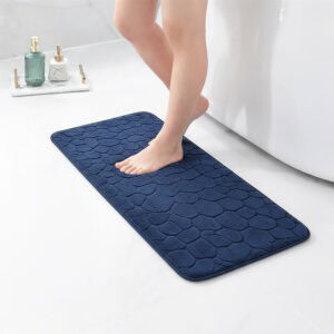 Barefoot stepping on a long navy blue runner mat with pebble texture placed on a bathroom tile floor next to a tub