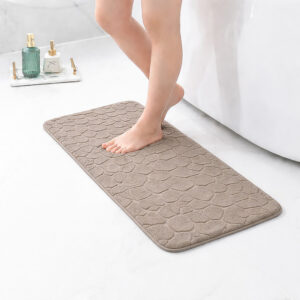 Barefoot stepping on a long taupe runner mat with pebble texture placed on a bathroom tile floor next to a tub