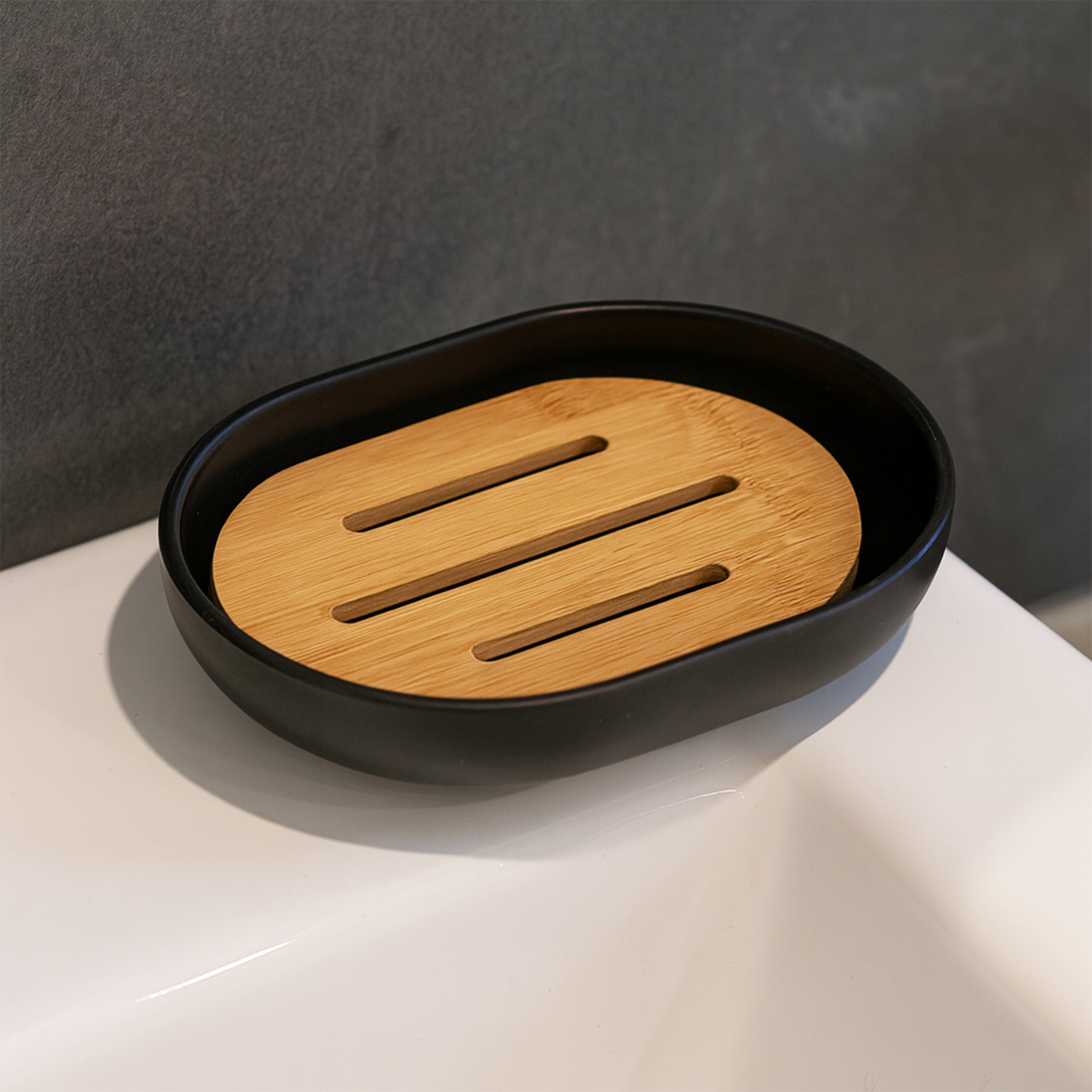 Empty black soap dish with bamboo insert on white sink surface