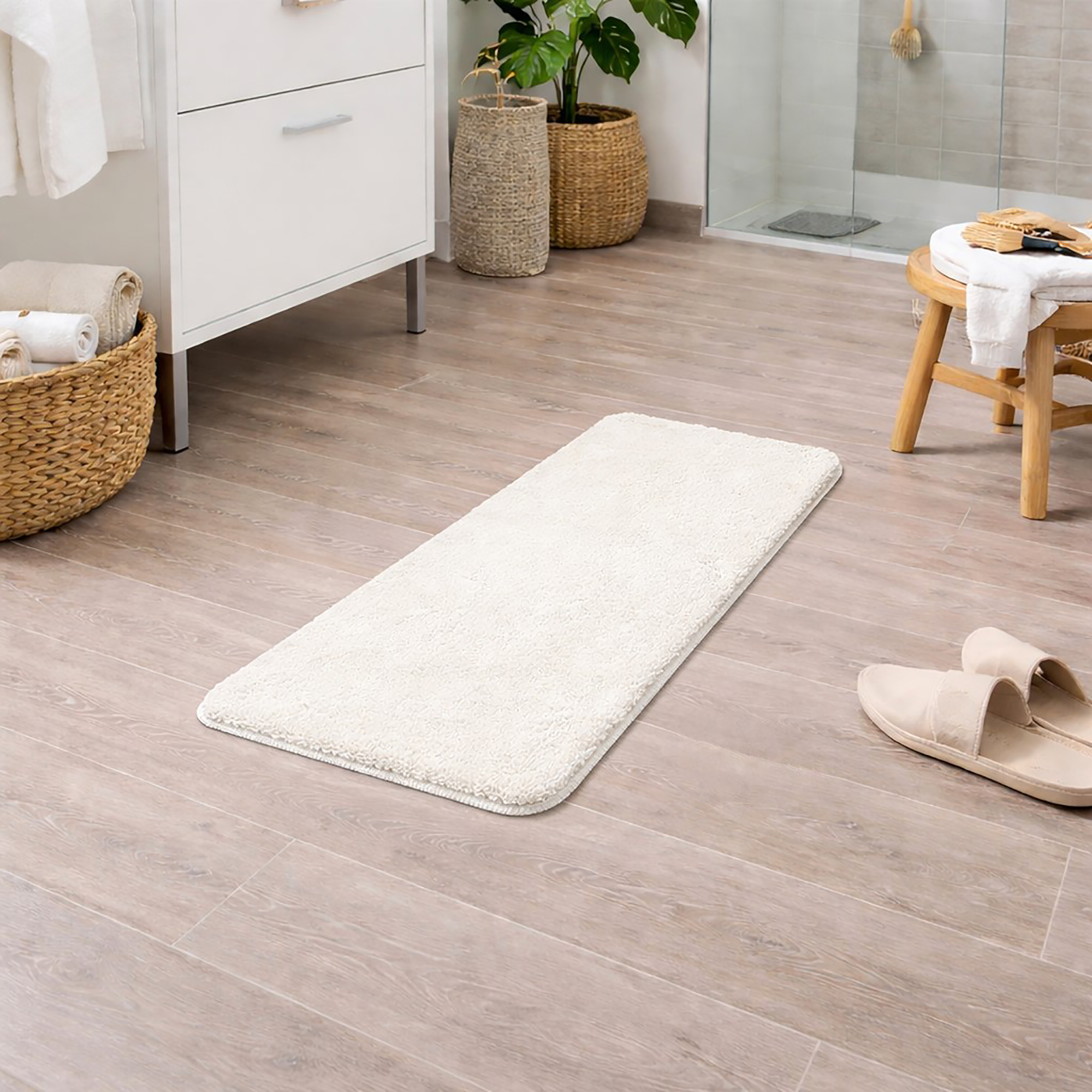 "Off-white microfiber bath mat runner on light wood bathroom floor with wicker baskets and plants"