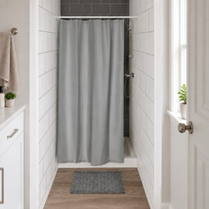 Gray half size shower curtain closing a narrow tiled shower stall in a small bright bathroom