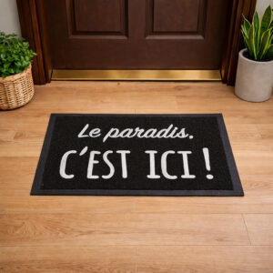 Lifestyle view of black Le paradis, c'est ici! door mat placed in front of wooden entry door