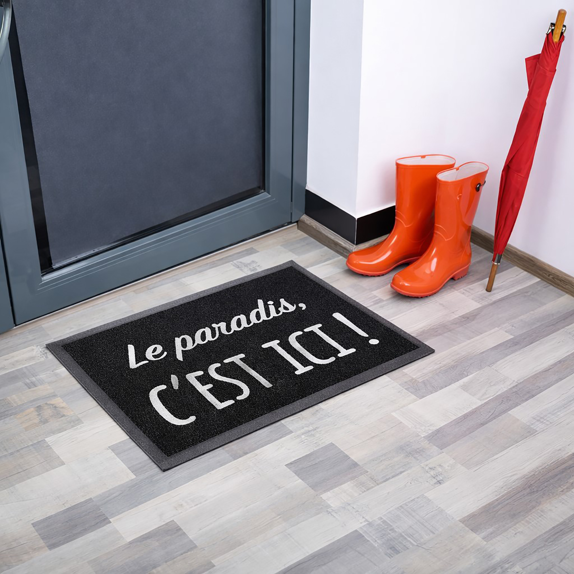 Angled indoor entryway view with black Le paradis, c'est ici! doormat boots and umbrella