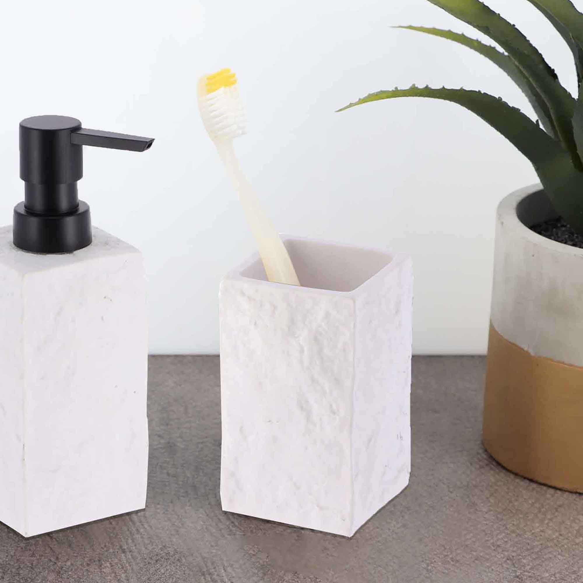 A white stone-effect bathroom tumbler holding a toothbrush, displayed alongside a matching soap dispenser and a small plant on a countertop.