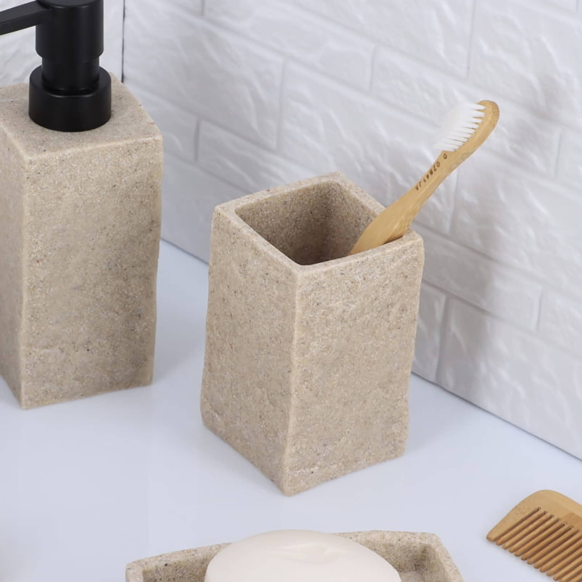 A natural stone-effect bathroom tumbler holding a toothbrush, displayed alongside a matching soap dispenser on a countertop.