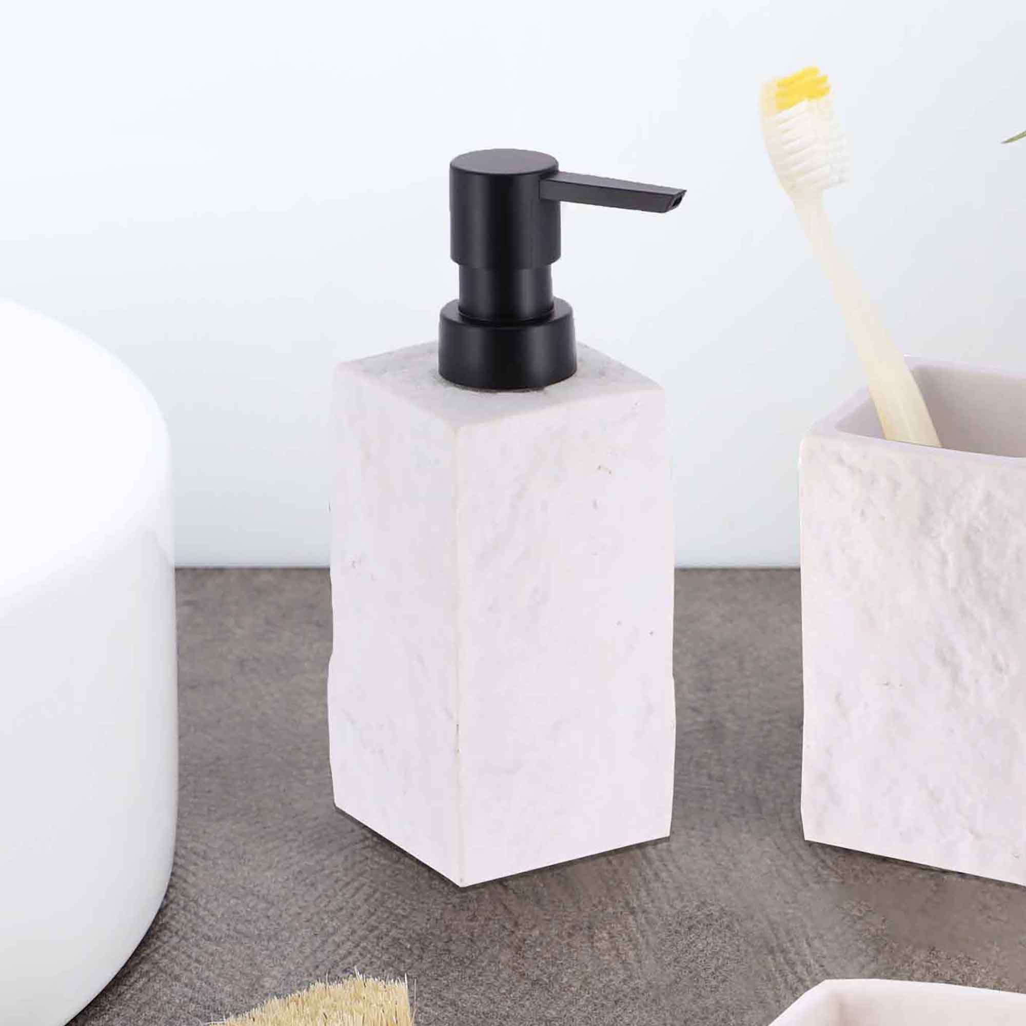 A white stone-effect soap dispenser with a black pump, displayed next to a matching toothbrush holder on a bathroom countertop.