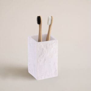 A white stone-effect bathroom tumbler holding two bamboo toothbrushes, displayed against a neutral background for a clean and natural look.