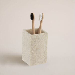 A natural stone-effect bathroom tumbler holding two bamboo toothbrushes, displayed against a neutral background for a clean and natural look.