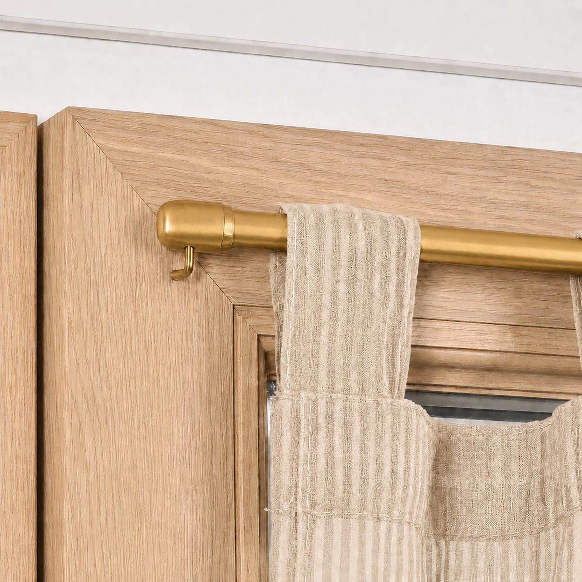 Gold cafe rod mounted on wood window frame with sheer curtain, close-up
