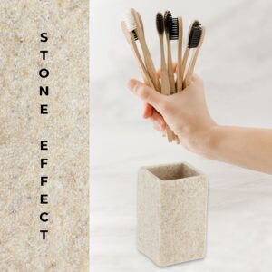 A close-up of a natural stone-effect bathroom tumbler next to a hand holding multiple bamboo toothbrushes, emphasizing its modern design and practicality.