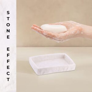 Hand holding bar soap above white stone effect soap dish
