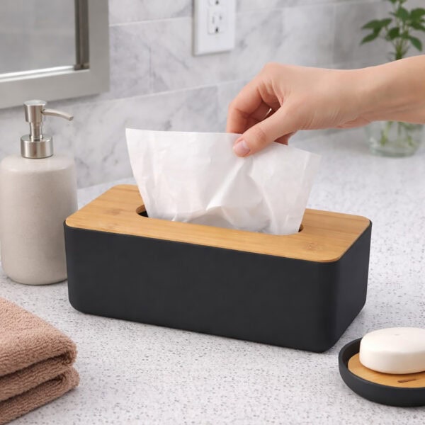 Hand pulling tissue from black rectangular tissue box with bamboo lid on bathroom counter