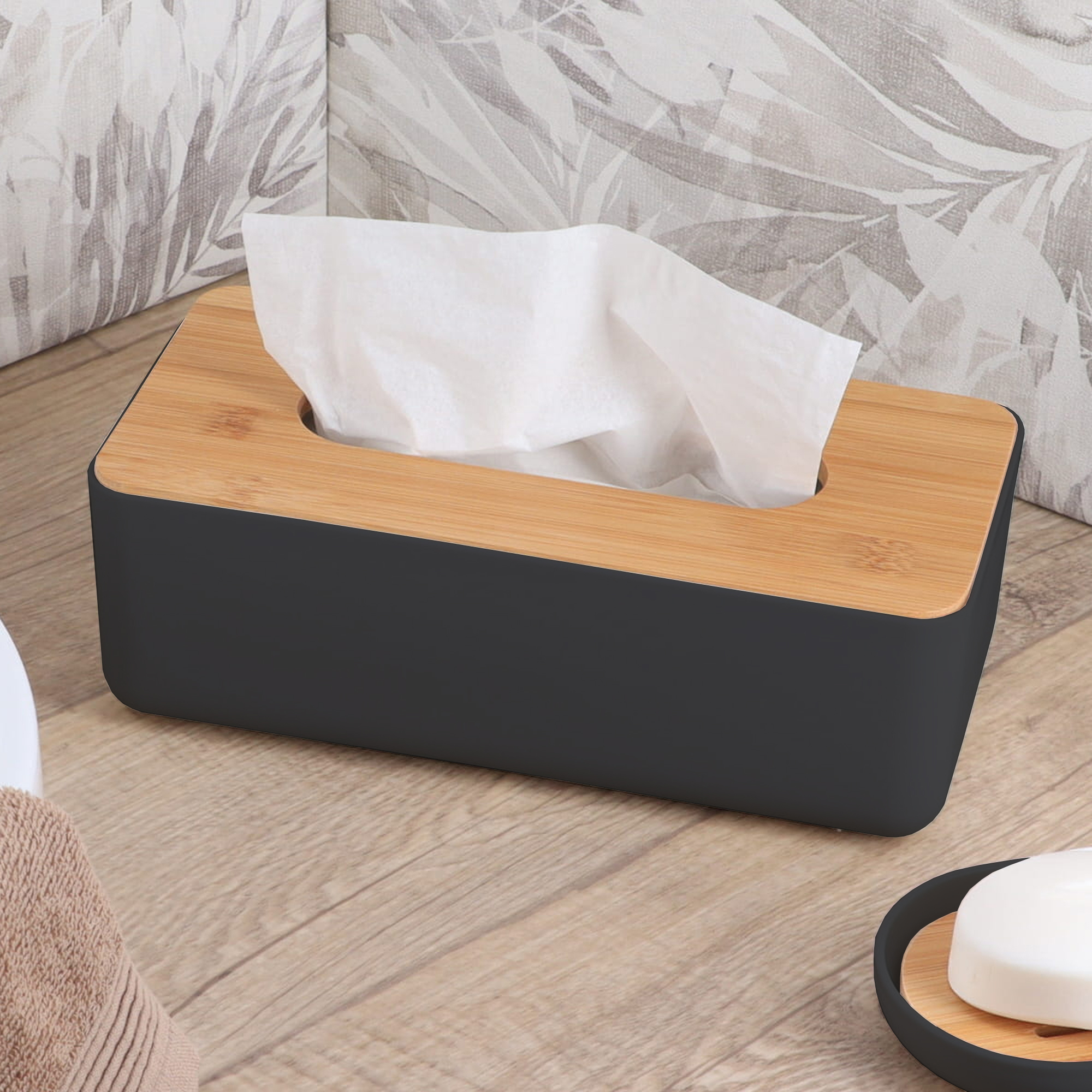 Black tissue box with bamboo lid on wooden surface with neutral leaf pattern pillows