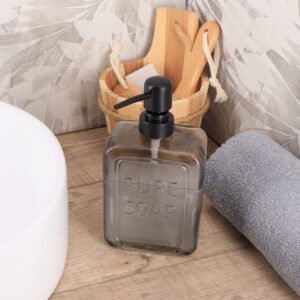 Smoked glass soap dispenser Pure Soap 18 fl oz on a wood bathroom floor beside a bathtub and folded towel