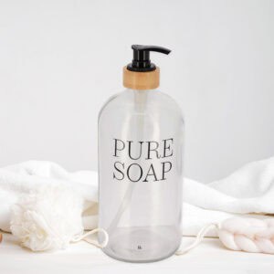 Clear glass soap dispenser with pure soap print styled on white surface with bath sponges
