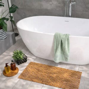 Bamboo bath mat placed beside white freestanding bathtub with green towel