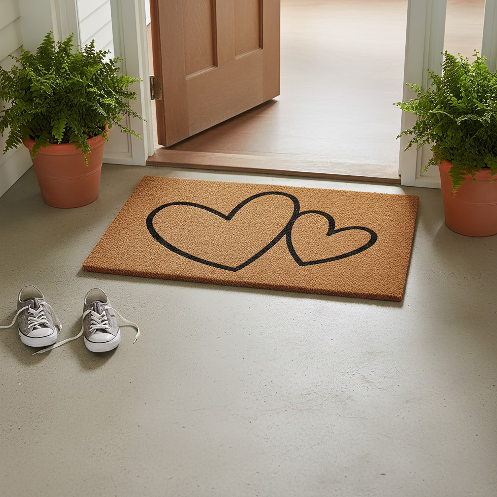 Hearts design coir doormat at open doorway with plants and sneakers