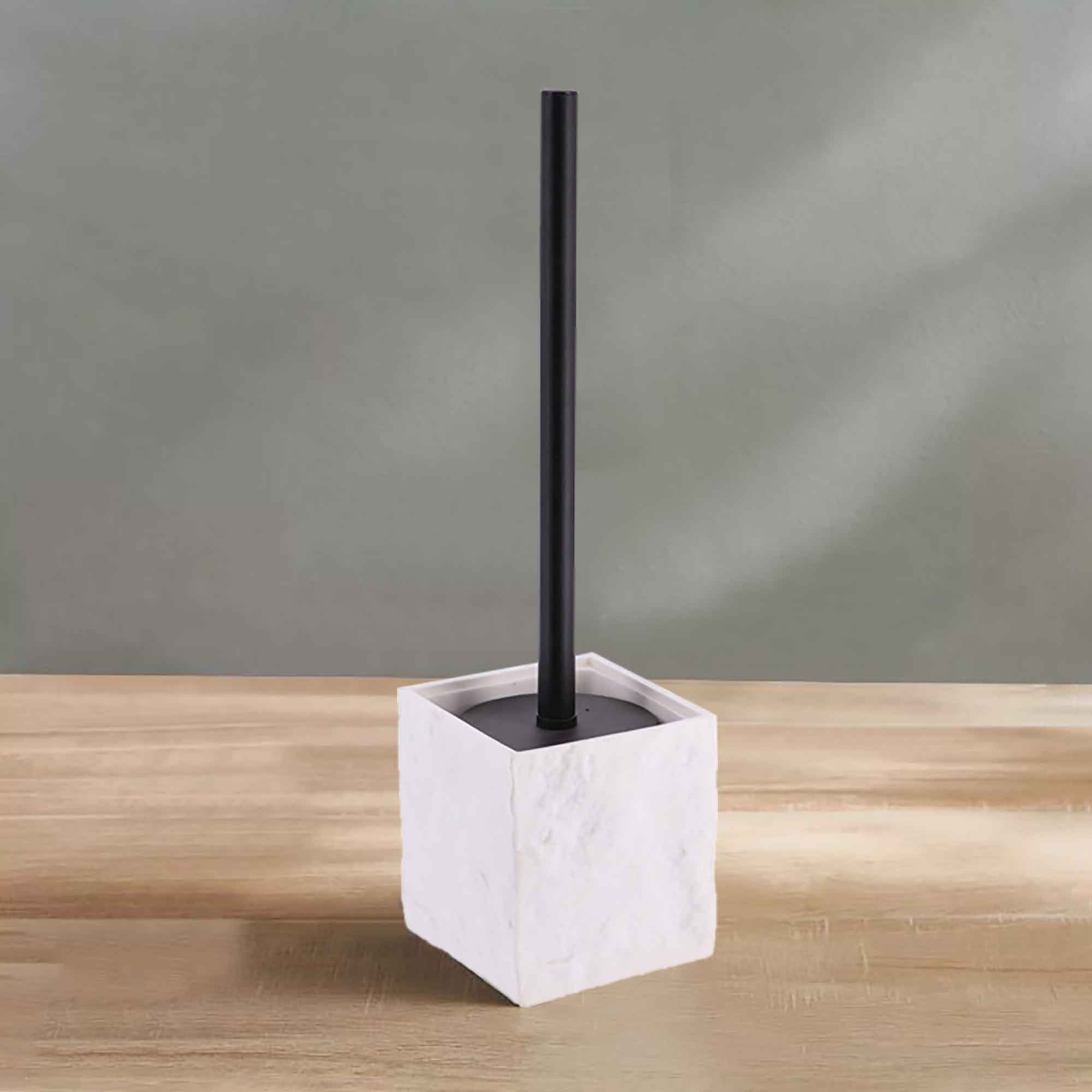 A white stone-effect toilet brush holder with a black handle, displayed on a wooden surface against a soft green wall for a clean aesthetic.