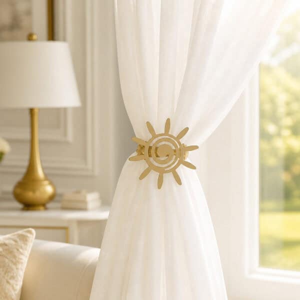 2- Cream sheer curtain held to one side by a matte gold sun tieback in an elegant living room with a gold lamp.