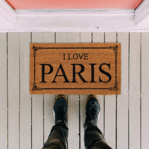 I Love Paris coir door mat on a white wooden porch, top view with feet in front, 24 x 13 inches