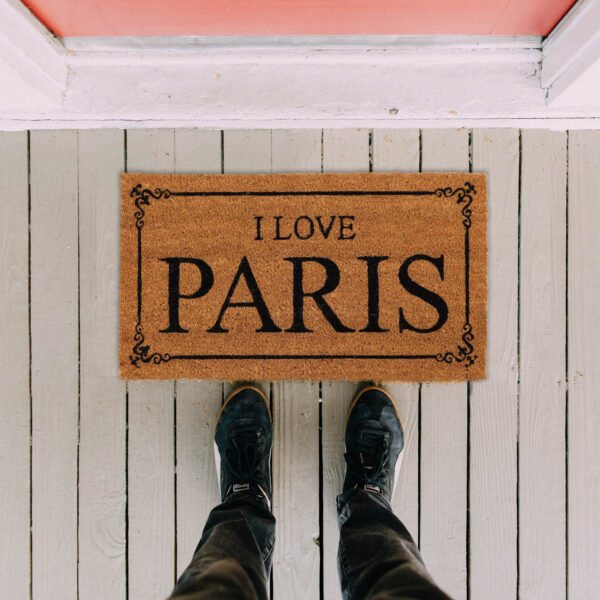I Love Paris coir door mat on a white wooden porch, top view with feet in front, 24 x 13 inches