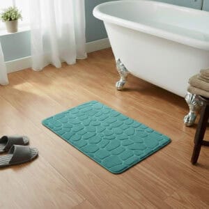 Peacock blue memory foam bath mat with embossed pebble stone texture on wooden floor beside clawfoot tub