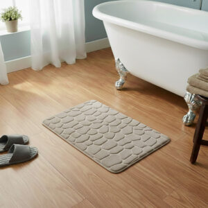 Taupe memory foam bath mat with embossed pebble stone texture on wooden floor beside clawfoot tub