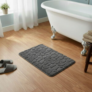 Dark gray memory foam bath mat with embossed pebble stone texture on wooden floor beside clawfoot tub