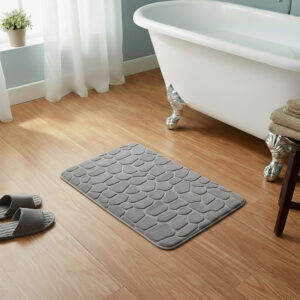 Light gray memory foam bath mat with embossed pebble stone texture on wooden floor beside clawfoot tub