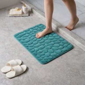 Barefoot stepping on a soft peacock blue pebble design memory foam mat placed on a bathroom tile floor