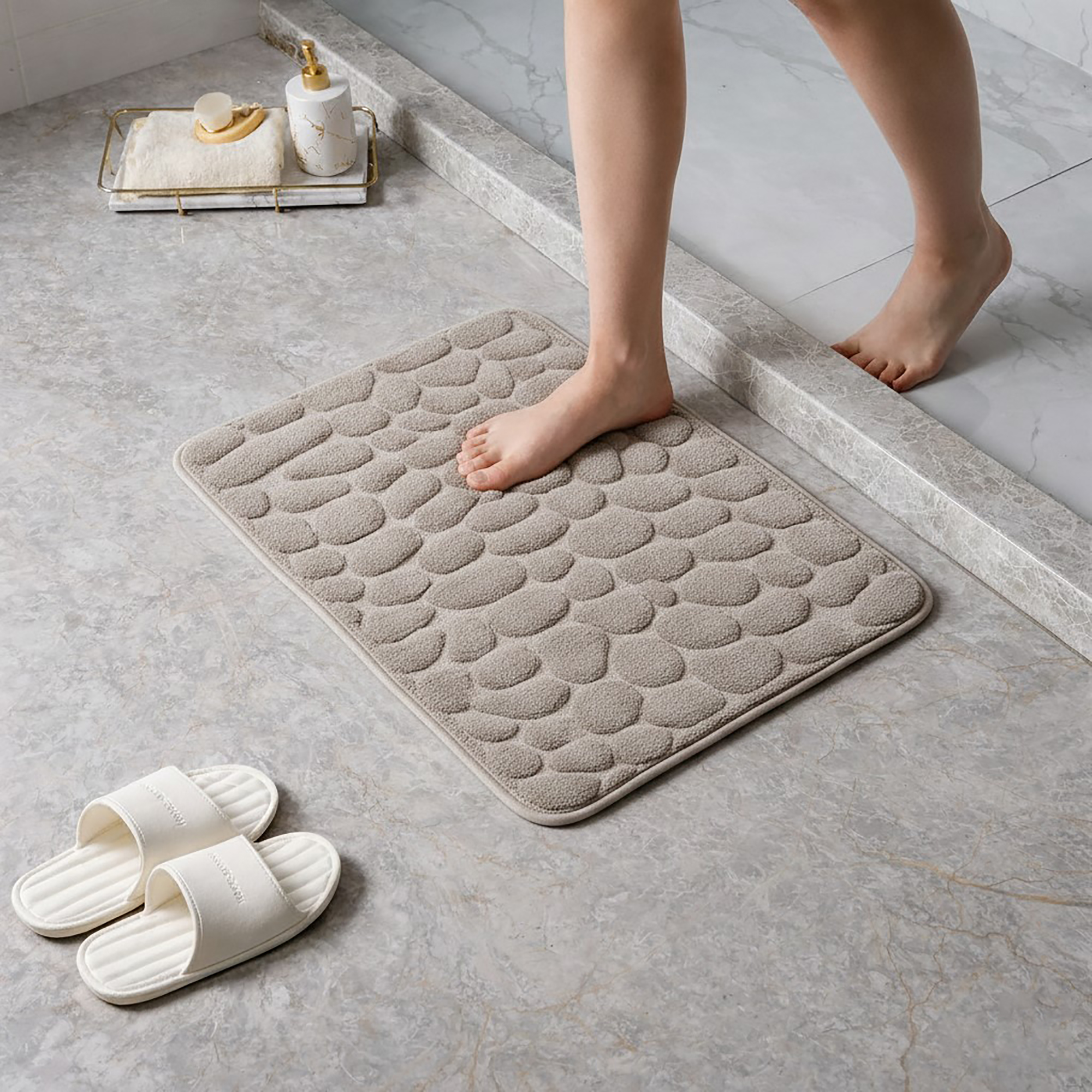 Barefoot stepping on a soft taupe pebble design memory foam mat placed on a bathroom tile floor