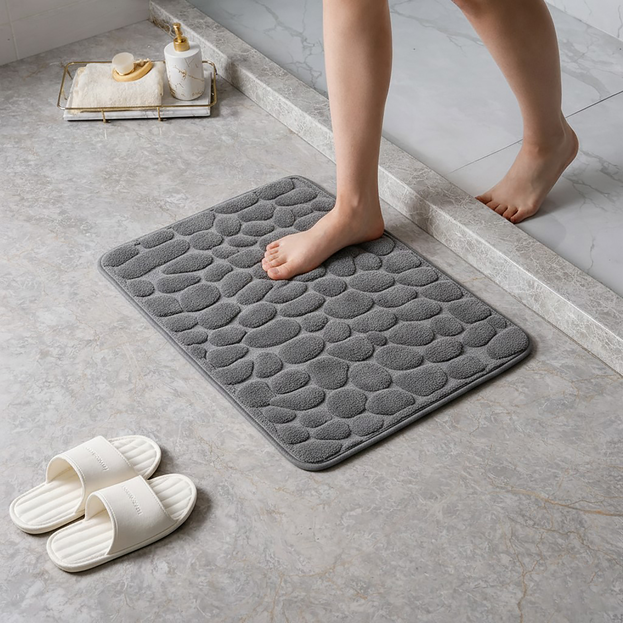 Barefoot stepping on a soft dark gray pebble design memory foam mat placed on a bathroom tile floor