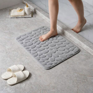 Barefoot stepping on a soft light gray pebble design memory foam mat placed on a bathroom tile floor