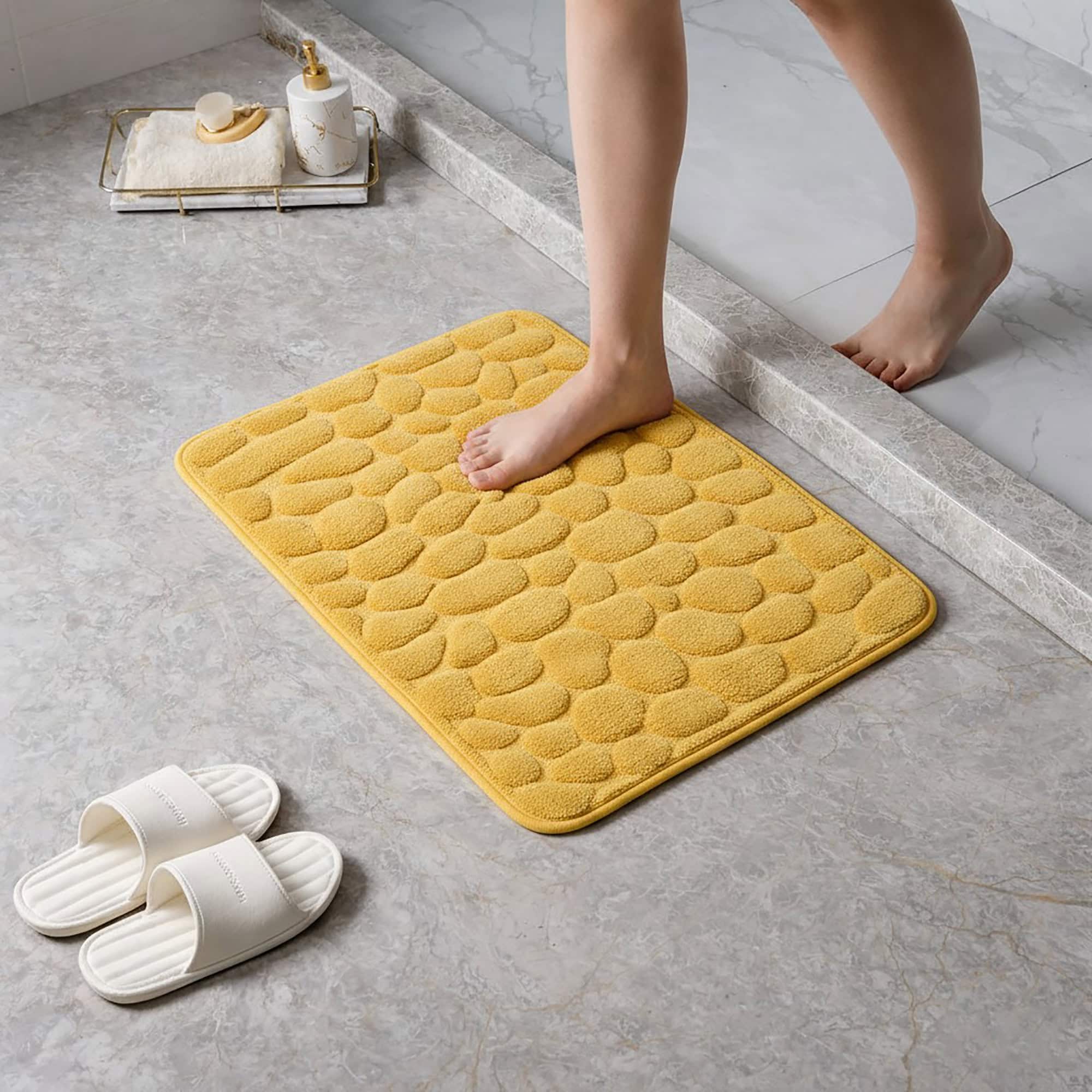 Barefoot stepping on a soft mustard yellow pebble design memory foam mat placed on a bathroom tile floor