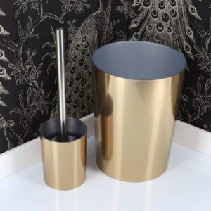 Brushed gold toilet brush holder and matching waste bin against black peacock feather wallpaper