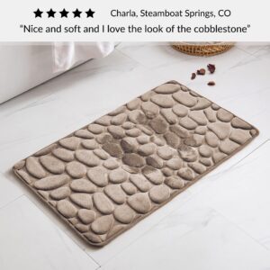 Taupe bath mat with cobblestone pattern placed near bathtub on bathroom floor with customer review praising softness and design