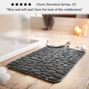 Dark gray bath mat with cobblestone pattern placed near shower on wood floor with customer review praising softness and design