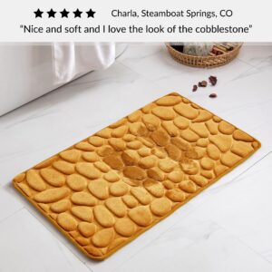 Mustard yellow bath mat with cobblestone pattern placed near bathtub on bathroom floor with customer review praising softness and design