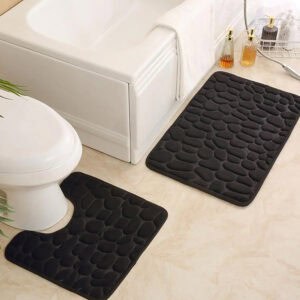 Black pebble bath mat set featuring standard and contour shapes placed around white tub and toilet on beige tile floor