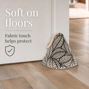Black leaf print cone door stopper propping open a white door on hardwood floor, with a shield icon. On-image text: "Soft on floors," "Fabric touch helps protect."
