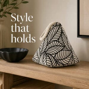 Black leaf print cone door stopper on a wooden console beside a black bowl, a vase, and framed art. On-image text: "Style that holds."