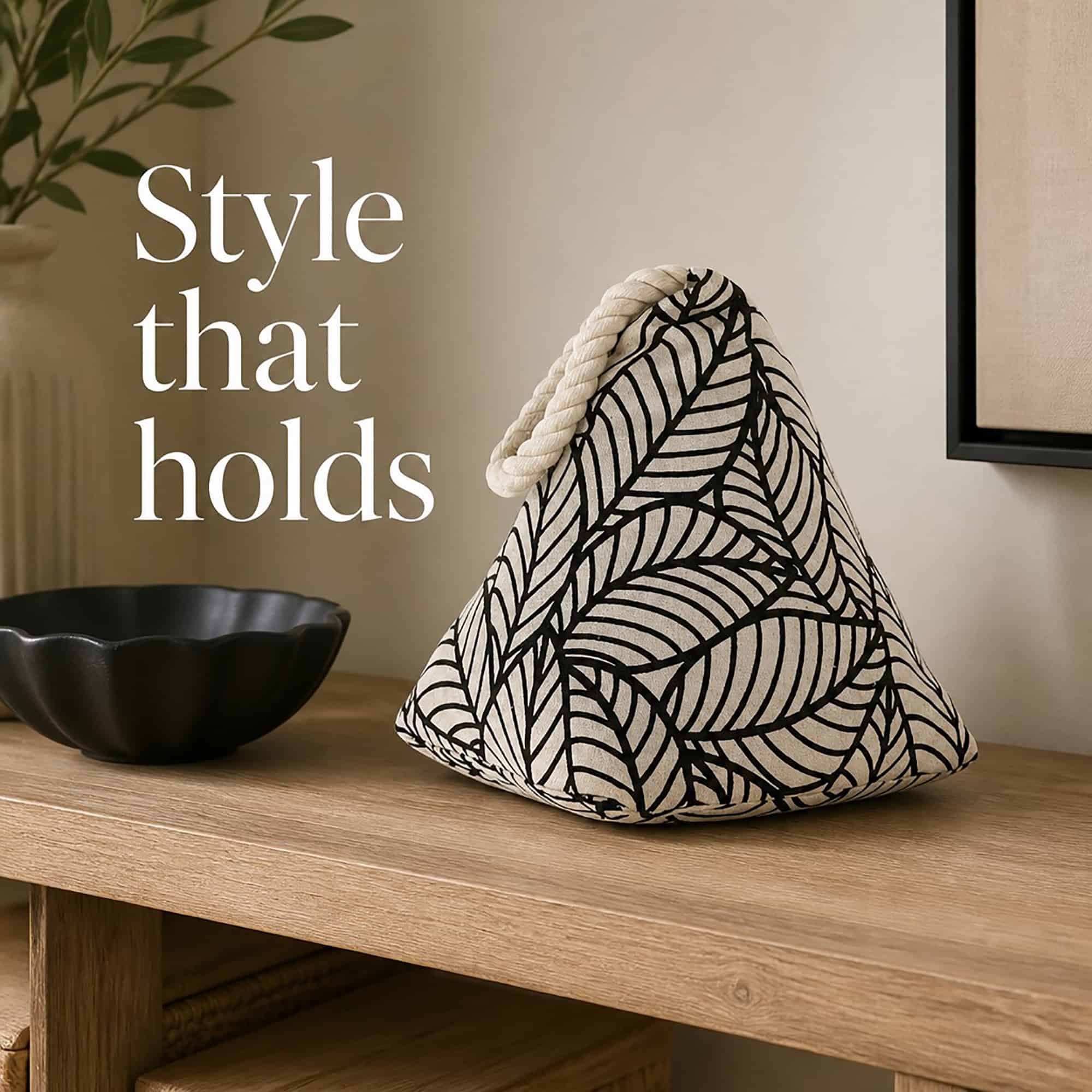 Black leaf print cone door stopper on a wooden console beside a black bowl, a vase, and framed art. On-image text: "Style that holds."