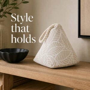 White leaf print cone door stopper on a wooden console beside a black bowl, a vase, and framed art. On-image text: "Style that holds."