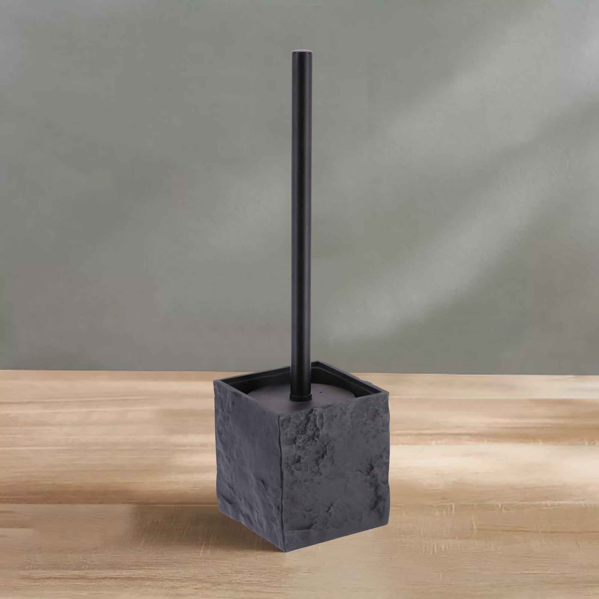 A black stone-effect toilet brush holder with a black handle, displayed on a wooden surface against a soft green wall for a clean aesthetic.