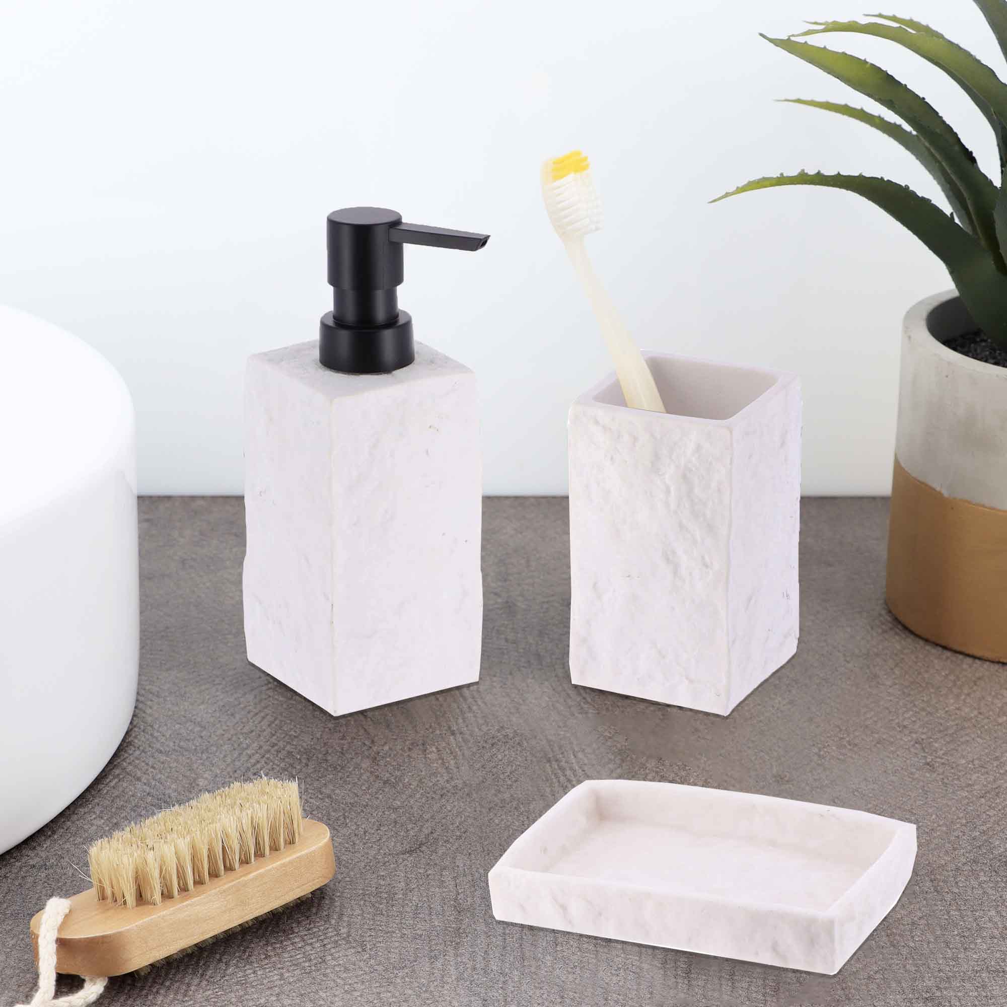 White stone-effect bathroom accessories, including a tumbler, soap dispenser, and soap dish, displayed on a countertop with a toothbrush and plant.