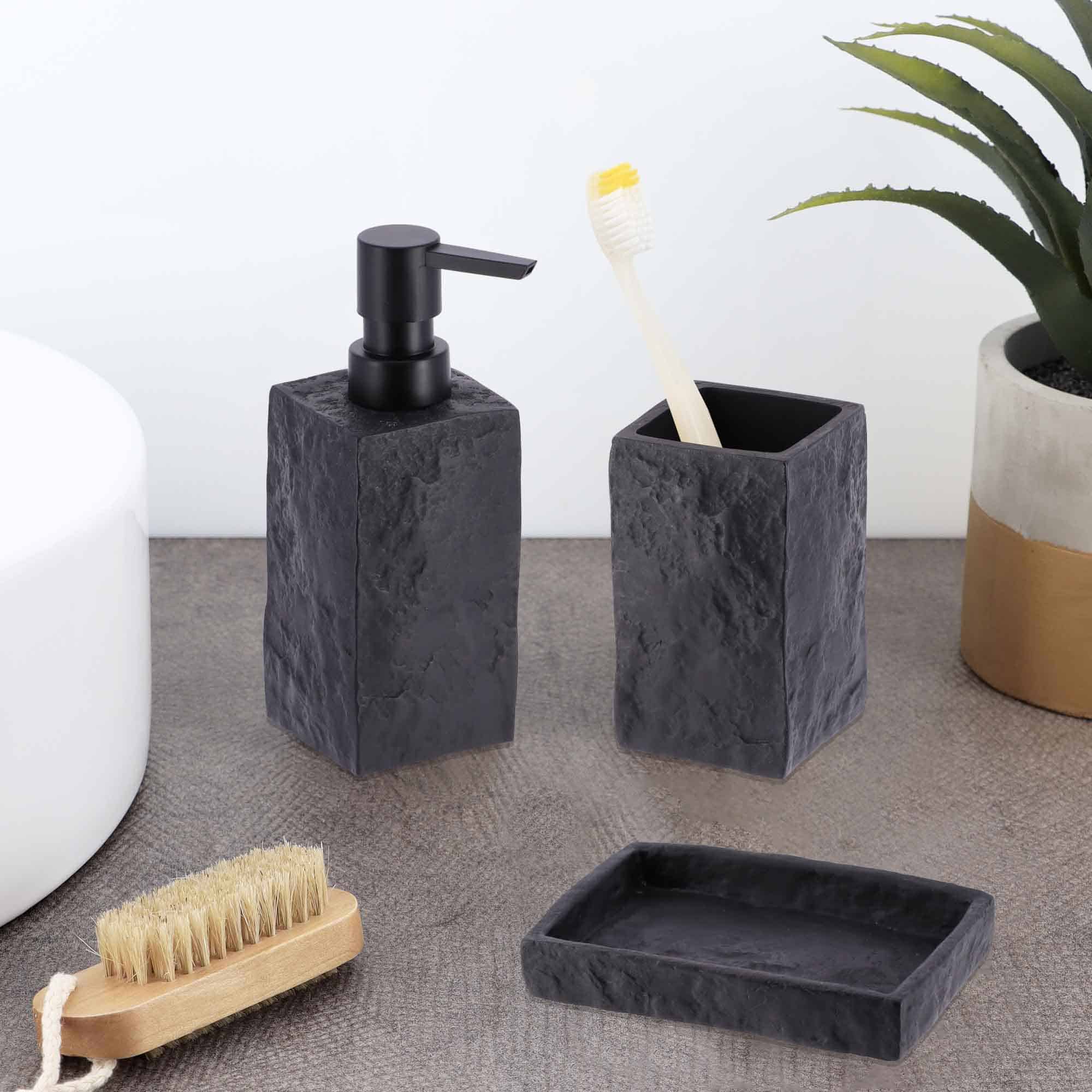 Black stone-effect bathroom accessories, including a tumbler, soap dispenser, and soap dish, displayed on a countertop with a toothbrush and plant.