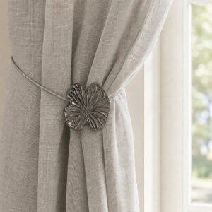Lifestyle grège: Polished graphite water lily magnetic tieback holding a light gray sheer linen curtain by a sunlit window
